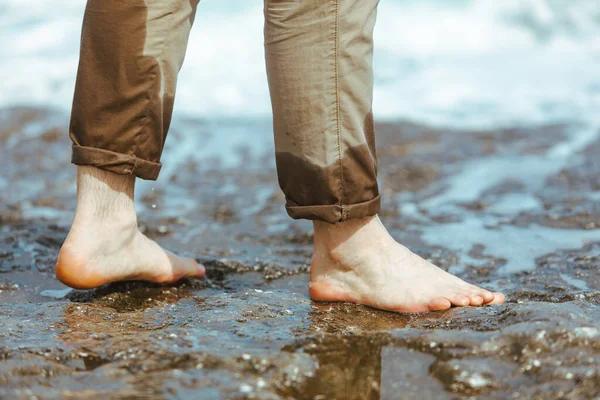 wet man legs in pants walking by sea rocky beach enjoying water. summer vacation