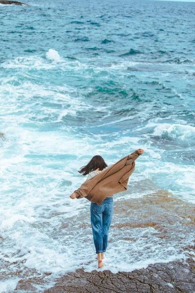woman walking by rocky beach in wet jeans barefoot. summer sea vacation