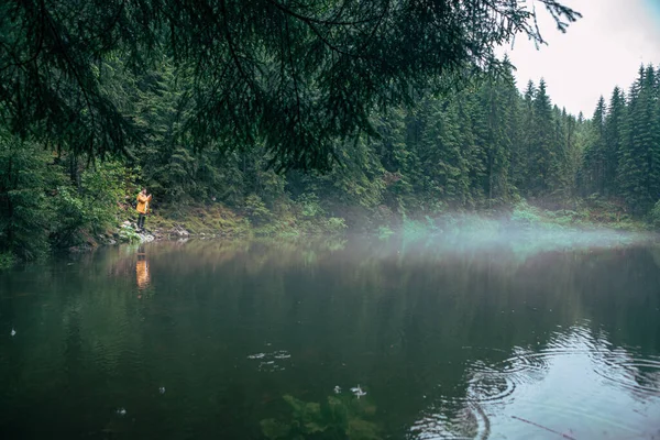 穿着黄色雨衣的徒步旅行者望着山湖游人的概念复制空间 — 图库照片