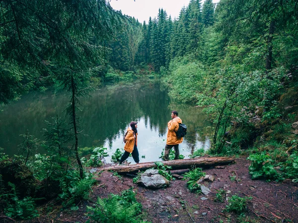 穿着黄色雨衣的徒步旅行者看着高山湖中的背包客 — 图库照片