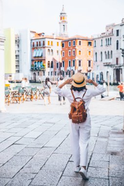 arkasından kahverengi deri sırt çantası görünümü ile beyaz giysiler içinde kadın