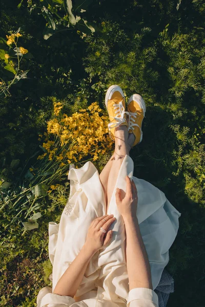 Mulher em sapatos amarelos sentado na grama perto de buquê de colza — Fotografia de Stock