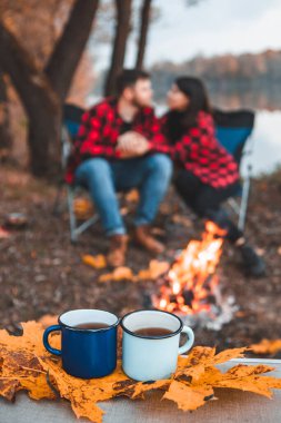 Fotokopi odasının arka planında, ateşin yanında bir adamla çay içen bir kadın.