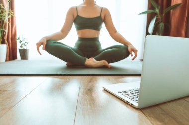 Kadın bilgisayarın yanında yoga yapıyor çevrimiçi öğrenim uzaktan spor eğitimi veriyor.