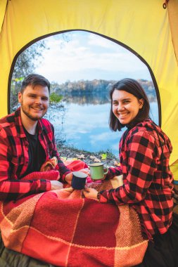 Çadırda oturup ılık çay içen çift sonbahar gölüne bakıyor. kamp konsepti