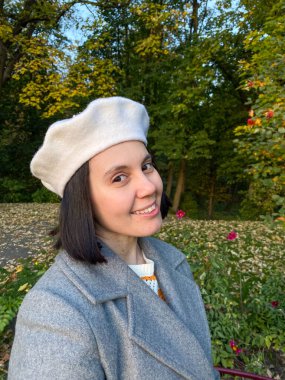 Gri paltolu ve bereli kadın gülen sonbahar parkında selfie çekiyor.