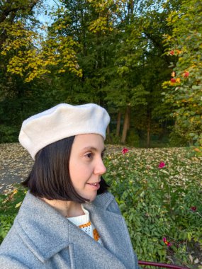 Gri paltolu ve bereli kadın gülen sonbahar parkında selfie çekiyor.