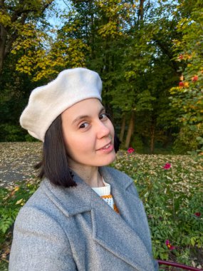 Gri paltolu ve bereli kadın gülen sonbahar parkında selfie çekiyor.