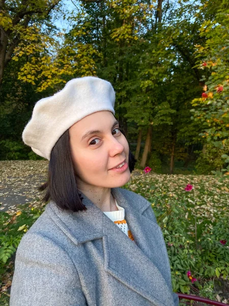 Gri paltolu ve bereli kadın gülen sonbahar parkında selfie çekiyor.