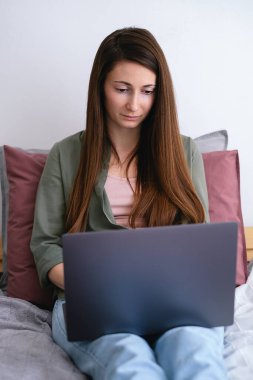 Yatakta dizüstü bilgisayarla çalışan serbest çalışan genç bir kadın. Uzak görev.