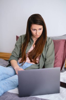 Yatakta dizüstü bilgisayarla çalışan konsantre kadın serbest yazar. Uzak görev.