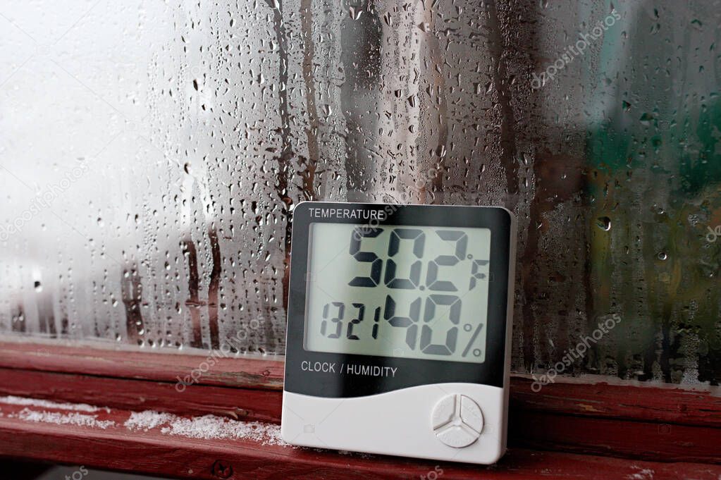 Electronic clock, calendar, thermometer, and hygrometer, against the background of condensation on glass, high humidity. Digital hygrometer in the laboratory shows the temperature of the pharyngeite