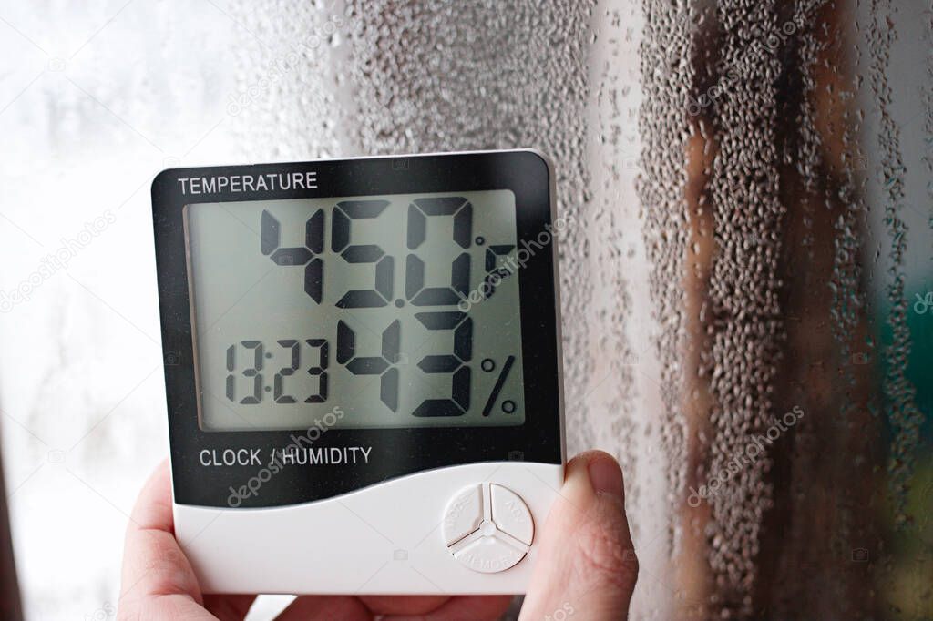 Electronic clock, calendar, thermometer, and hygrometer, against the background of condensation on glass, high humidity. Digital hygrometer in the laboratory shows the temperature of the pharyngeite