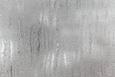 Camdan aşağı doğal su damlaları akıyor, odada nem oranı yüksek, cam camda buğulanma var. Tarafsız renkler. Yoğunlaşma damlaları dokusu ile mükemmel bir arka plan. Fotoğrafın yatay yönelimi