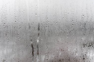 Camdan aşağı doğal su damlaları akıyor, odada nem oranı yüksek, cam camda buğulanma var. Tarafsız renkler. Yoğunlaşma damlaları dokusu ile mükemmel bir arka plan. Fotoğrafın yatay yönelimi