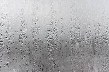 Camdan aşağı doğal su damlaları akıyor, odada nem oranı yüksek, cam camda buğulanma var. Tarafsız renkler. Yoğunlaşma damlaları dokusu ile mükemmel bir arka plan. Fotoğrafın yatay yönelimi
