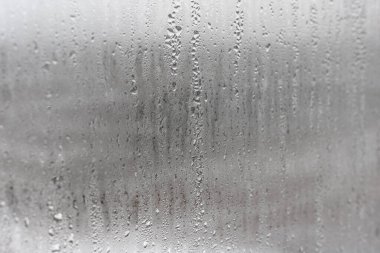 Camdan aşağı doğal su damlaları akıyor, odada nem oranı yüksek, cam camda buğulanma var. Tarafsız renkler. Yoğunlaşma damlaları dokusu ile mükemmel bir arka plan. Fotoğrafın yatay yönelimi