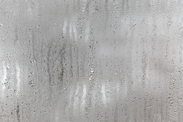 Natural drops of water flow down the glass, high humidity in the room, condensation on the glass window. Neutral colors. Excellent background with condensation drops texture. Horizontal orientation of the photo