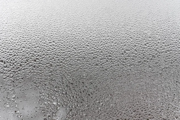 Natural drops of water flow down the glass, high humidity in the room, condensation on the glass window. Neutral colors. Excellent background with condensation drops texture. Horizontal orientation of the photo