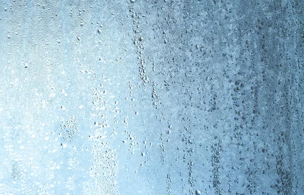 Natural frozen drops of condensation on transparent glass. Beautiful background from a frozen window in winter. Drops texture on the glass