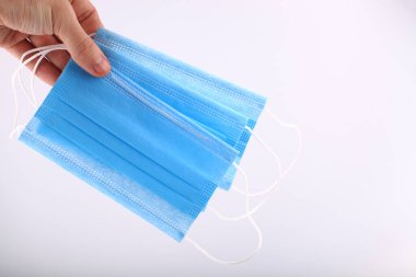 Beyaz arka planda mavi cerrahi maske tutan bir erkek. Pandemik korona virüsü, sigorta, hava hastalıkları, SARS, Grippe. İnsanlar için tıbbi maskeler burun ve ağzını kapatır.