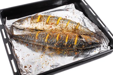 Baharatlı folyo ve limon dilimleri ile pişirmeye hazır iki çiğ deniz balığı.