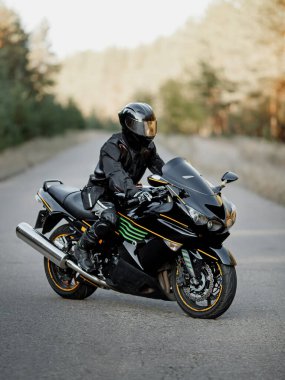 Kasklı siyah motosiklet sürücüsü bulanık arka planlı yolda