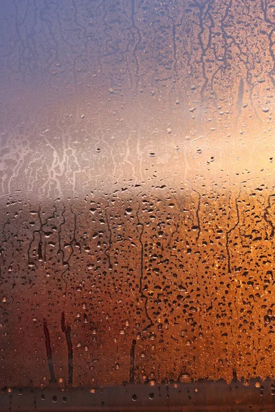 Drops of condensate on the sweaty glass window. Cold foggy glass. Wet window background, texture condensation with dripping drops