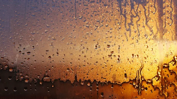 Drops of condensate on the sweaty glass window. Cold foggy glass. Wet window background, texture condensation with dripping drops