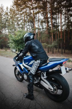 Kasklı ve deri kıyafetli siyah motosiklet sürücüsü.