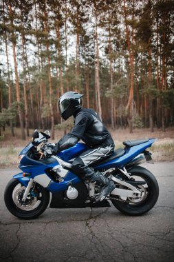 Siyah koruyucu takım elbiseli ve kasklı bisikletçi spor motosikletinin üstünde oturuyor.