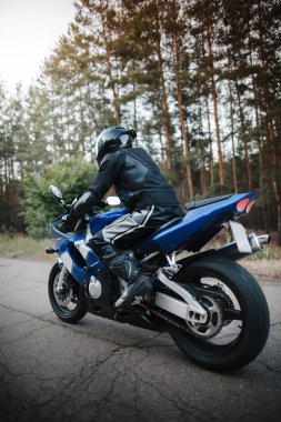 Motosiklet sürücüsünün arka görüntüsü bulanık orman arka planına sahip kaskla sürüşü