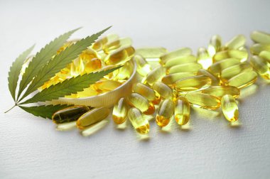 Kenevir CBD kapsülleri, yaprakları, CBD kenevir yağı kapsülleri içeren, kopyalama alanı olan beyaz bir tıbbi kenevir ürünüdür.