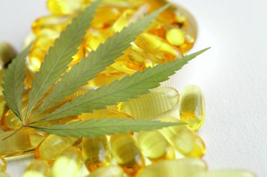 Kenevir CBD kapsülleri, yaprakları, CBD kenevir yağı kapsülleri içeren, kopyalama alanı olan beyaz bir tıbbi kenevir ürünüdür.