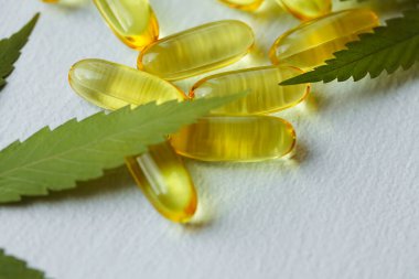 Beyaz arka planda esrarın temel yağ kapsülleri. CBD yağ kapsülleri ve kenevir yaprakları