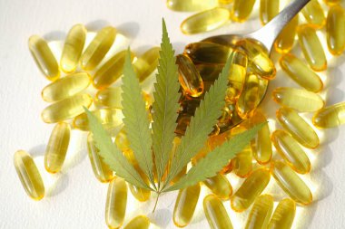 Beyaz arka planda esrarın temel yağ kapsülleri. CBD yağ kapsülleri ve kenevir yaprakları