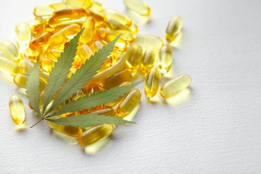 Beyaz arka planda esrarın temel yağ kapsülleri. CBD yağ kapsülleri ve kenevir yaprakları