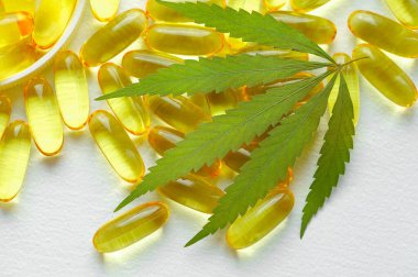 Beyaz arka planda esrarın temel yağ kapsülleri. CBD yağ kapsülleri ve kenevir yaprakları