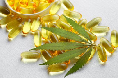 Beyaz arka planda esrarın temel yağ kapsülleri. CBD yağ kapsülleri ve kenevir yaprakları