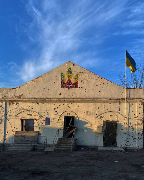 Богородичное, Донецкая область, Украина 23 февраля 2023 года: Полностью разрушенное село после российской оккупации, с поврежденным войной зданием, украинским флагом и национальной эмблемой, символизирующей освобождение.