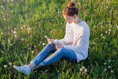 Çimenlerin üzerinde oturan ve tablet bilgisayar arayan kız