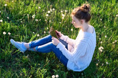 Çimenlerin üzerinde oturan ve tablet bilgisayar arayan kız