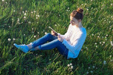 Çimenlerin üzerinde oturan ve tablet bilgisayar arayan kız