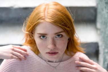 Merdivenlerin üzerinde duran ve kameraya bakarak Kızıl saçlı kız