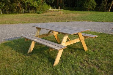 Çimenli bir alanda oturan ahşap piknik masası, doğanın güzelliğinin ortasında yemeğin tadını çıkarmak için mükemmel bir yer sağlıyor.