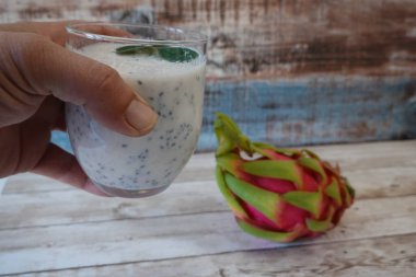 Elinde naneyle süslenmiş bir bardak chia pudingi taşralı ahşap bir masada taze ejderha meyvesiyle.