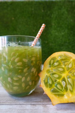 Bir bardak kiwano suyunun yanında dilimlenmiş boynuzlu kavun ve sağlıklı bir içecek için portakal çizgili kamış.