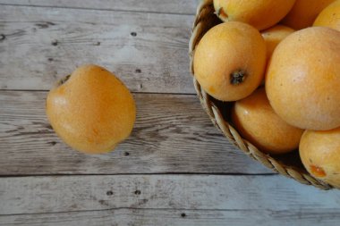 Olgun lokuatlar hasır bir sepetten dökülüp yıpranmış ahşap bir masaya dökülüp büyüleyici bir natürmort oluşturur.