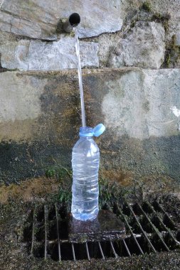 Şeffaf plastik su şişesi, açık taştan bir fıskiyenin içindeki küçük metal bir oyuktan taze ve temiz su akışıyla doluyor.