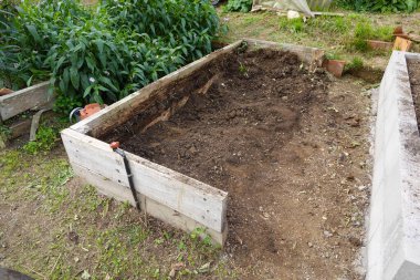 Toprakla dolu, sebze ekmeye hazır ahşap bahçe yatağı. Beton blok yatağı yeni inşaatı gösteriyor